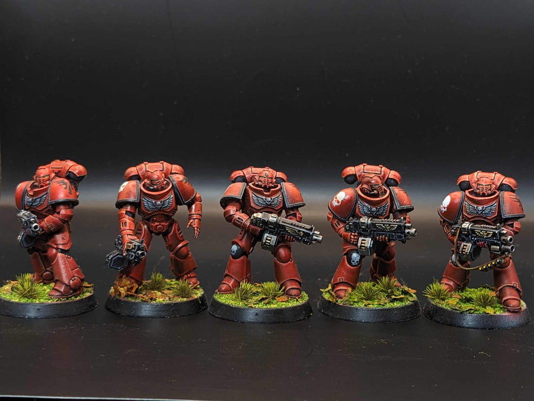 Five detailed red Space Marine miniatures in power armor, each armed and posed on grassy bases.