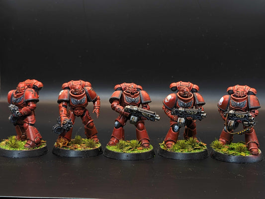 Five detailed red Space Marine miniatures in power armor, each armed and posed on grassy bases.
