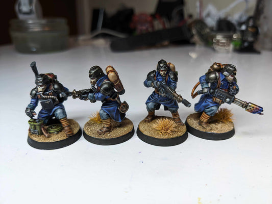 Four detailed resin miniatures of soldiers in blue uniforms, each wielding different weapons, on a sandy base.