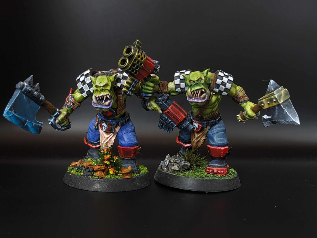Two meticulously painted orc miniatures with unique weapons and details on a dark background.