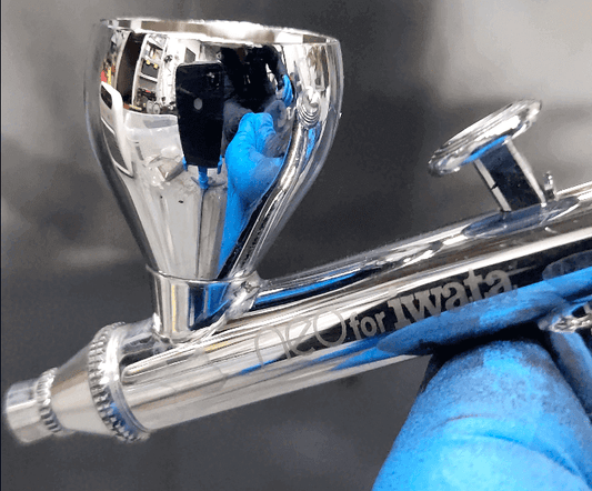 Close-up of an airbrush for painting miniatures, showcasing its shiny metal body and precise detailing.