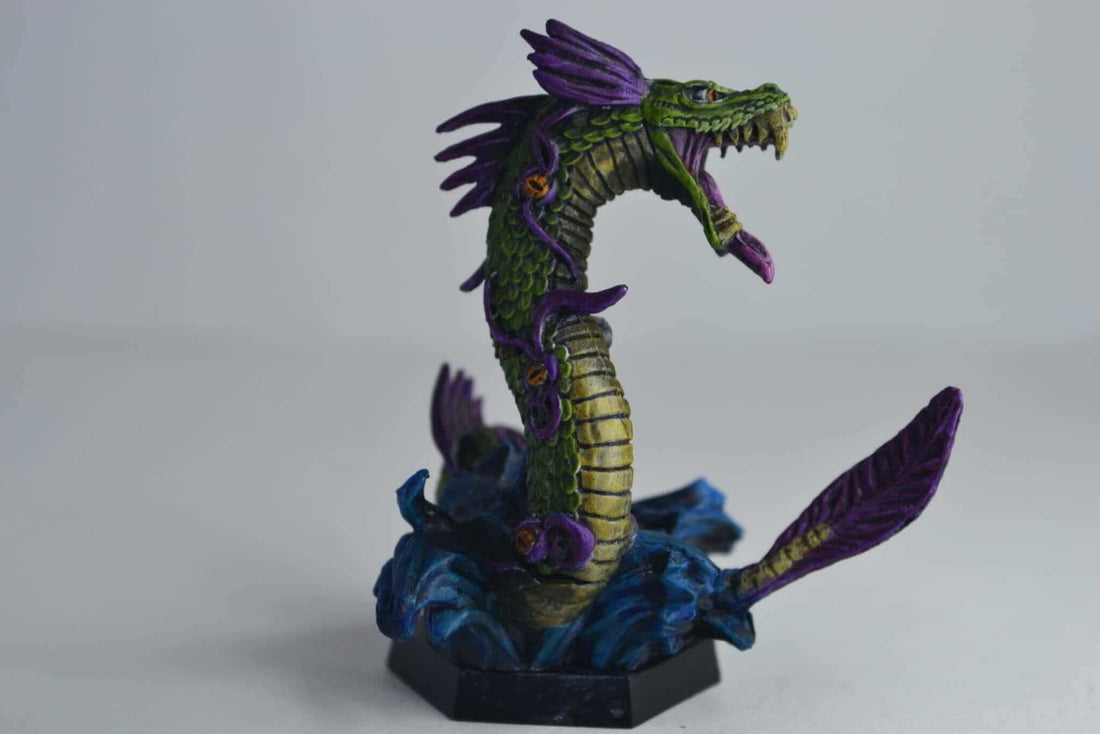 Vibrant green and purple dragon miniature on a blue base, showcasing detailed commission painting.